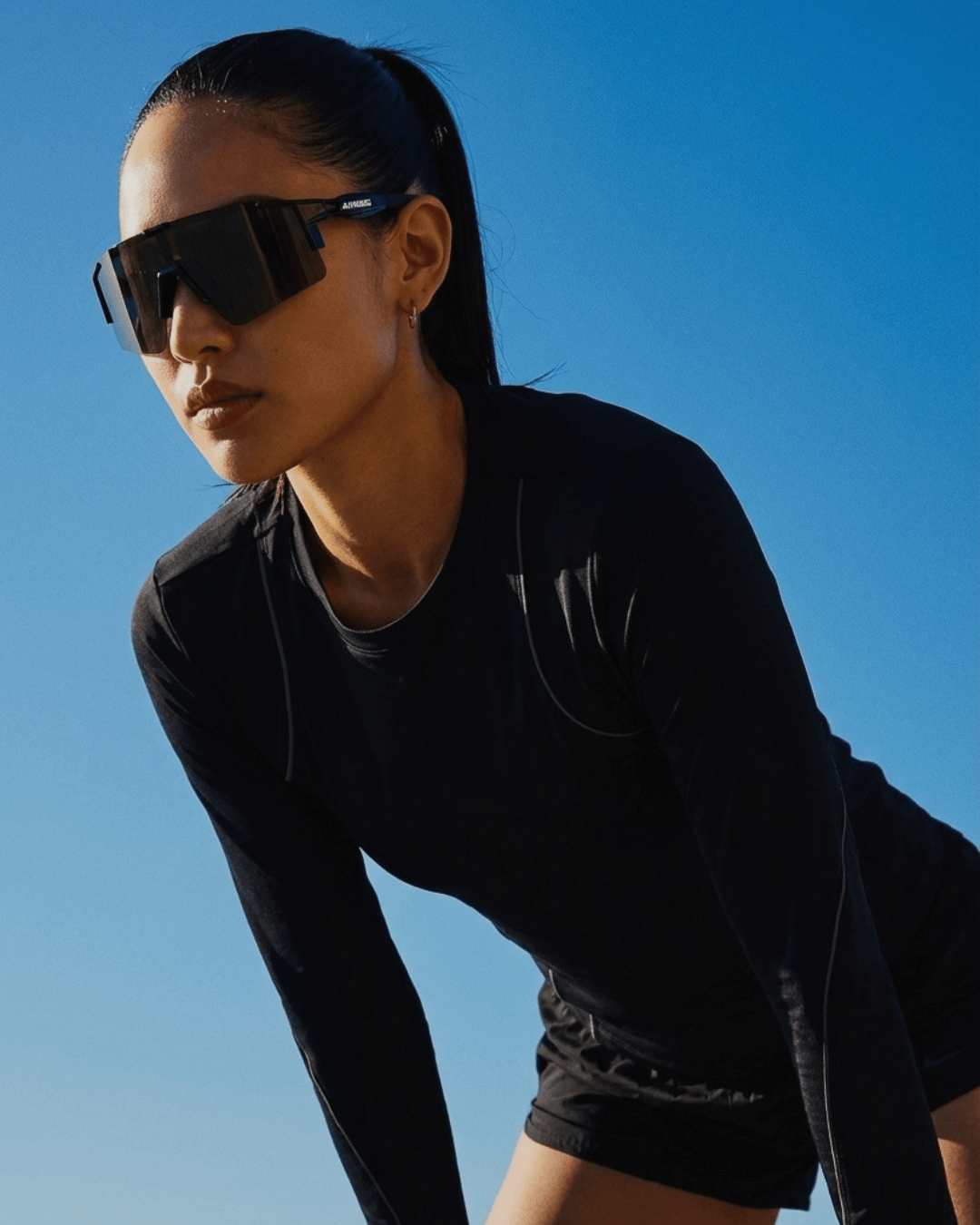 Person wearing blackout x365 sunglasses and black athletic outfit against a clear blue sky