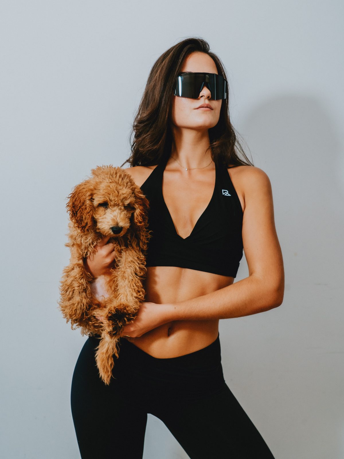 Woman in black leggings and sports bra holding a brown poodle puppy