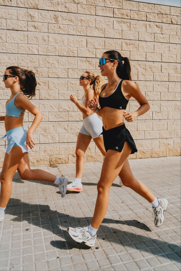 Three women running in Flyaway split running shorts and sports bras on a city street