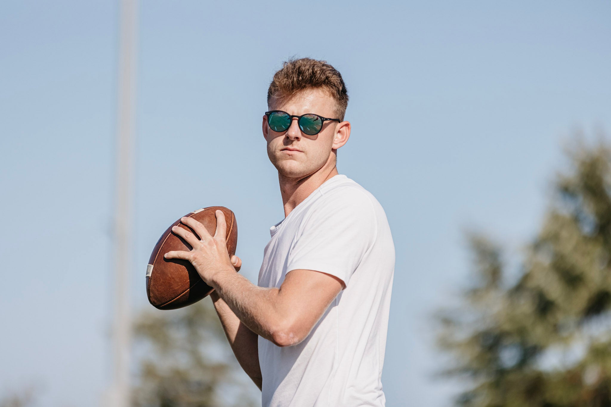 Man holding a football with olympian sunglasses against a clear sky