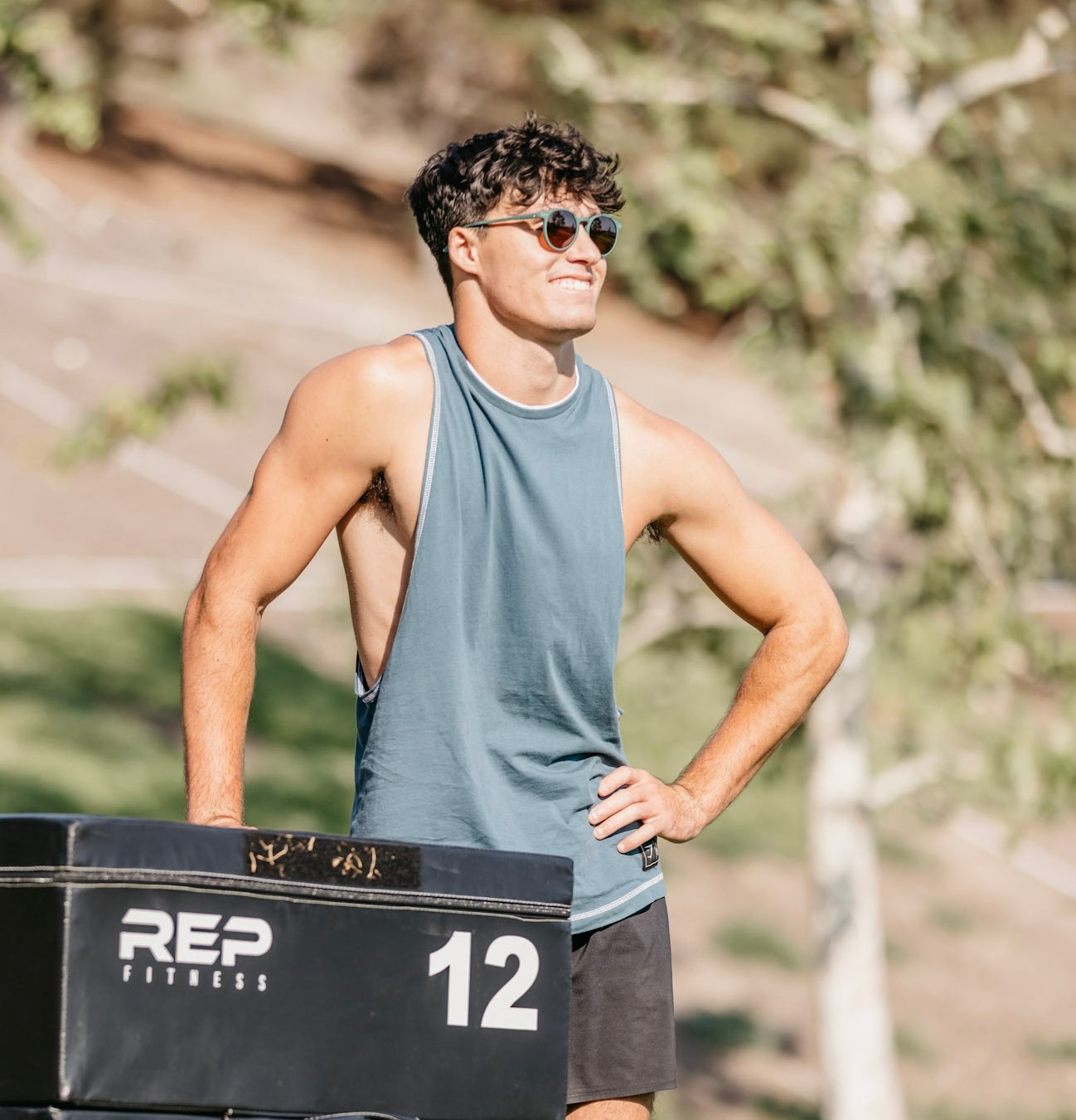 Man in a gray tank top and olympians sunglasses.