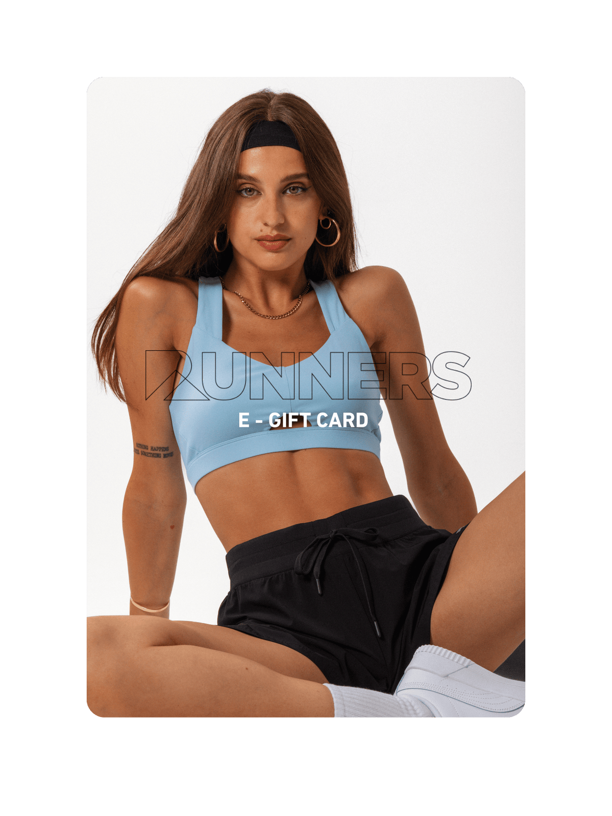 A woman in a sports bra and shorts sits against a white backdrop.