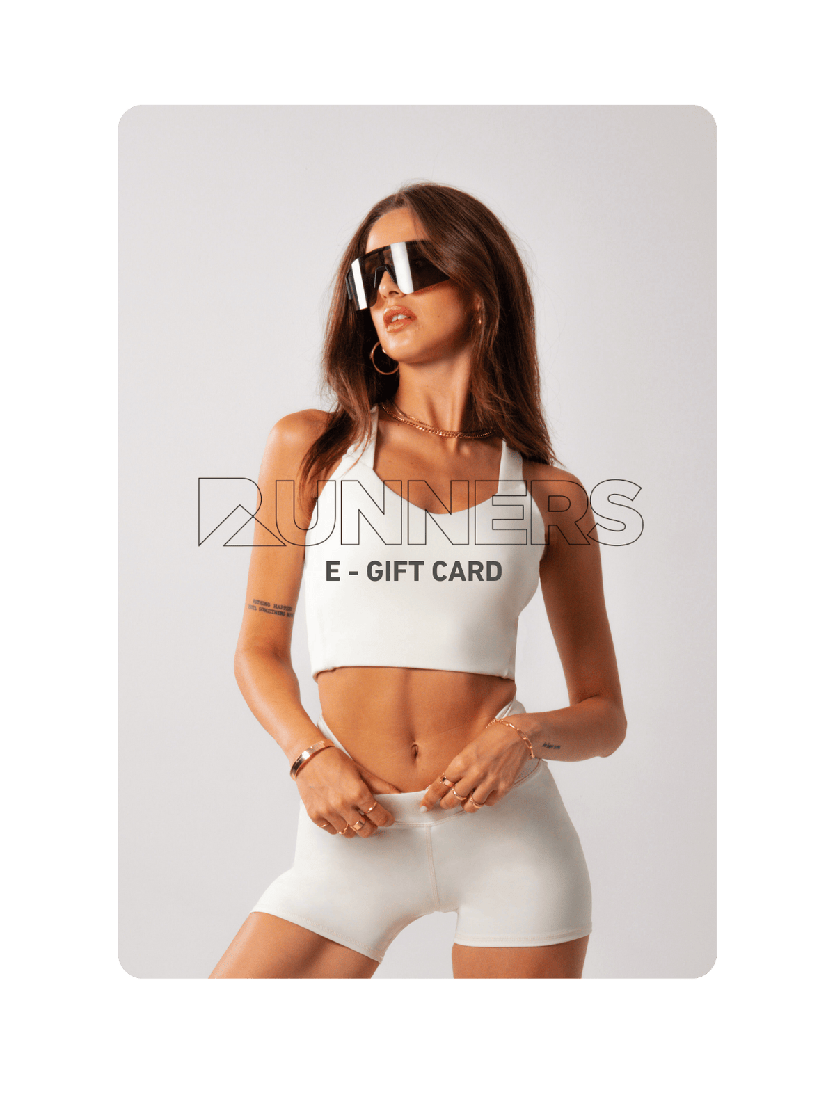 Woman in sunglasses, white crop top, and shorts. Gold jewelry. White background.