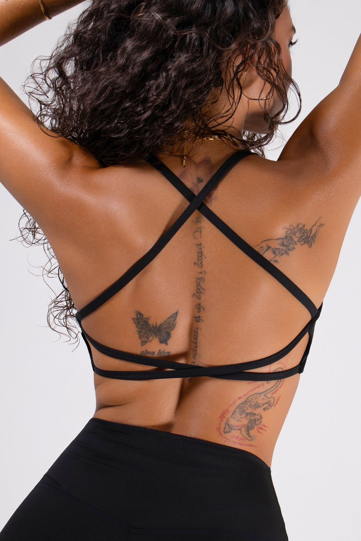 Runner's Athletics - Model in back view wearing black criss-cross strappy bra with tattoos