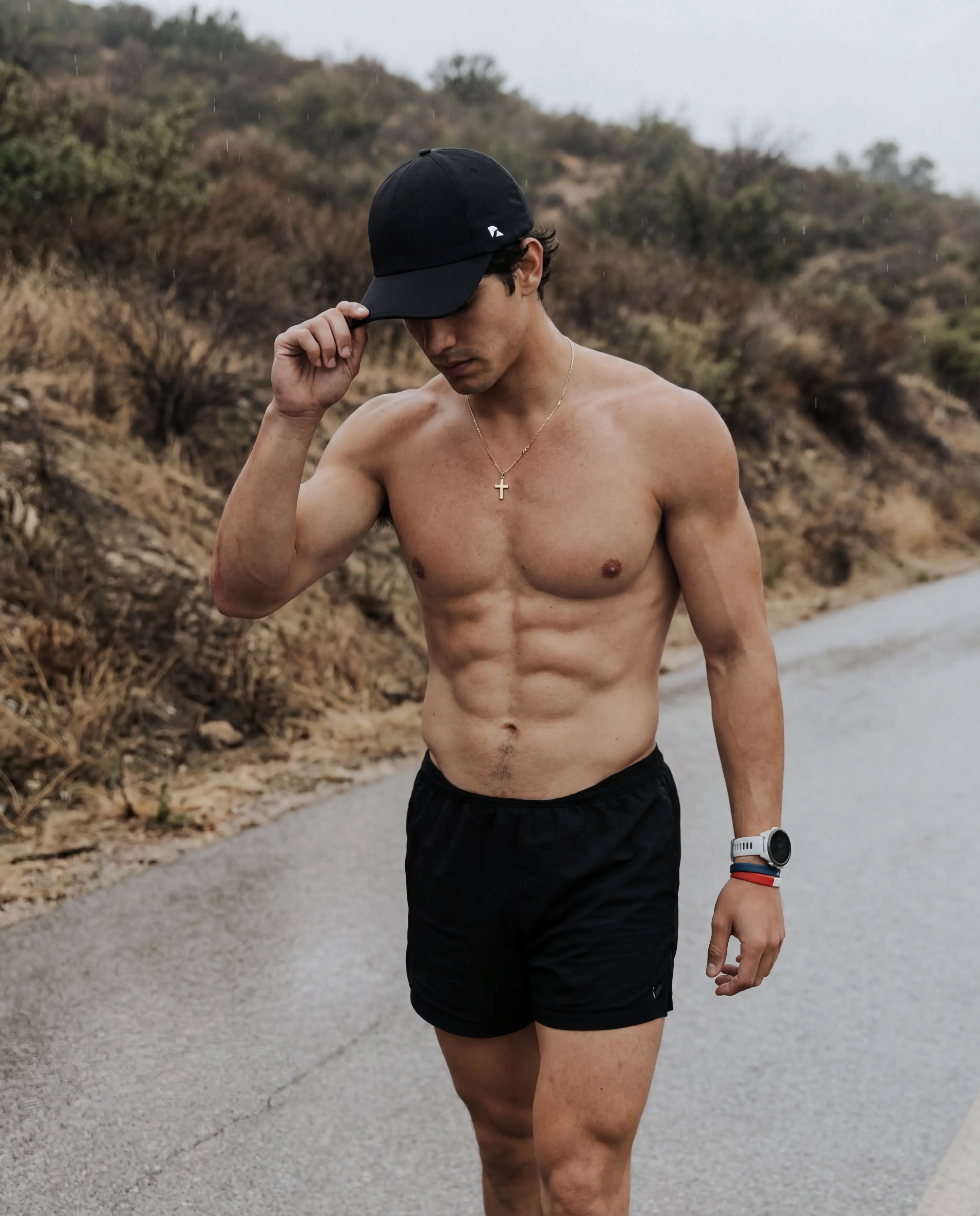 Black running hat with moisture-wicking fit worn by man in black athletic shorts during outdoor run