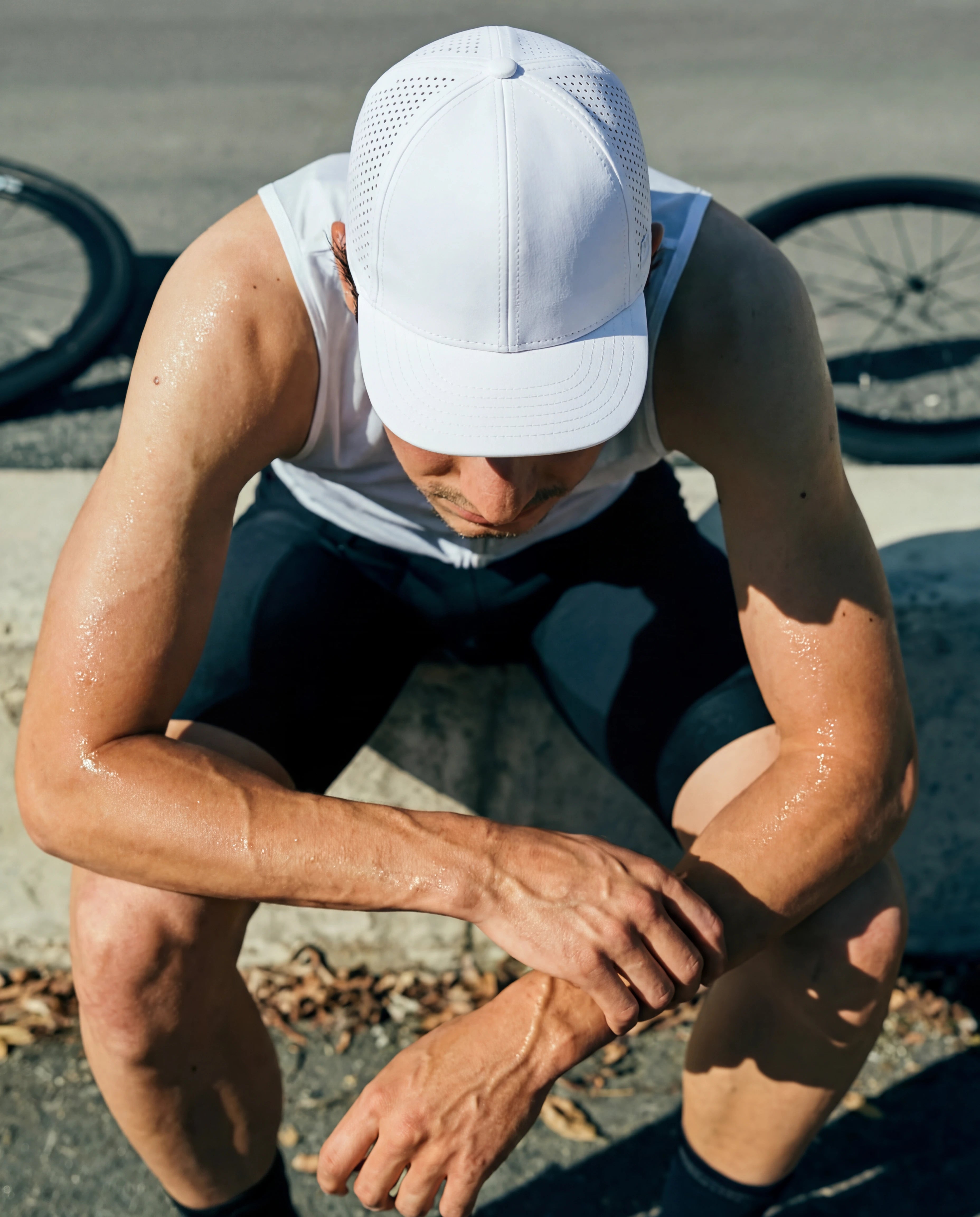 White perforated running hat on man resting post-workout in white tank and navy shorts from Runners Athletics