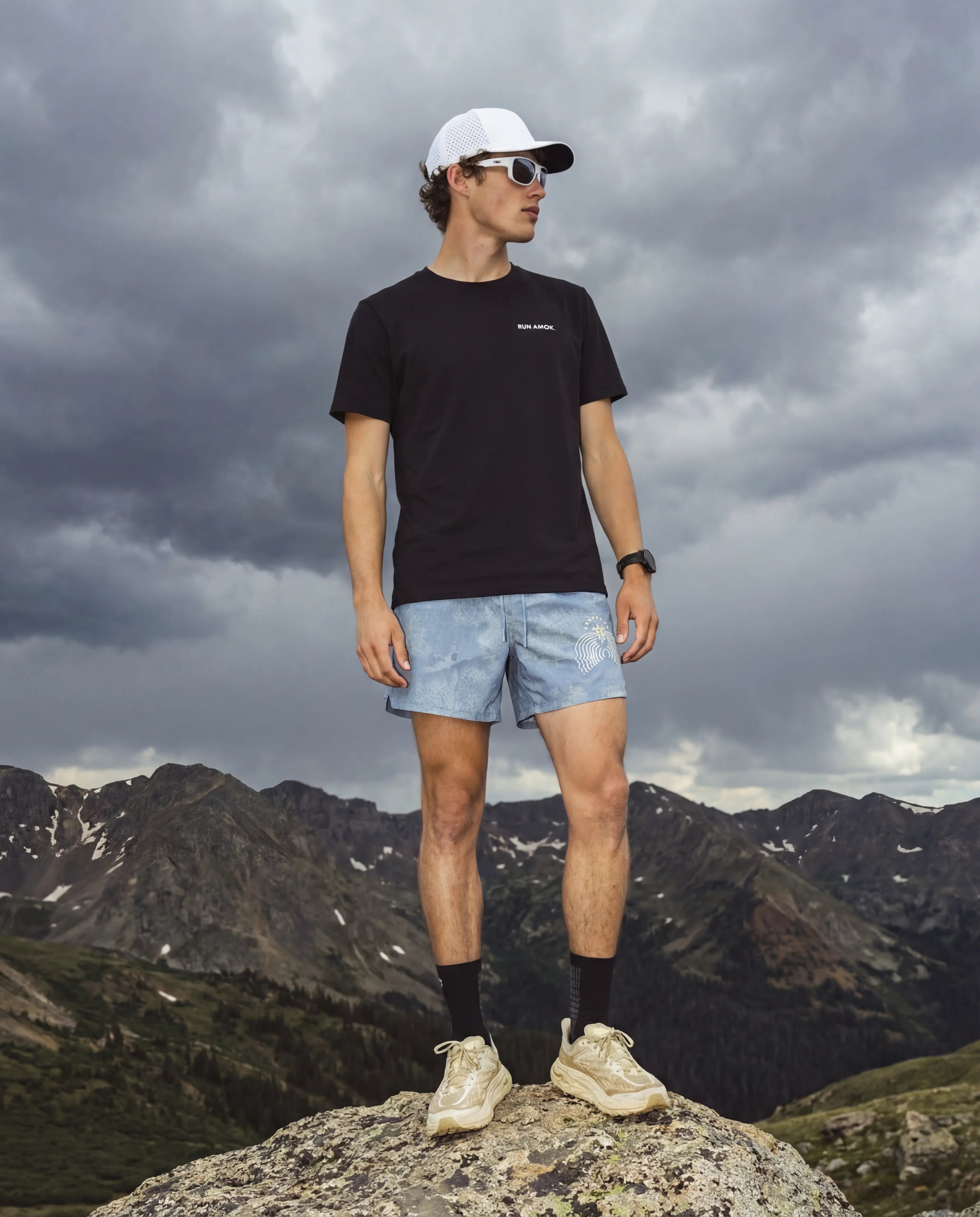 White running hat and wraparound running sunglasses on man in black tee and light blue shorts outdoors