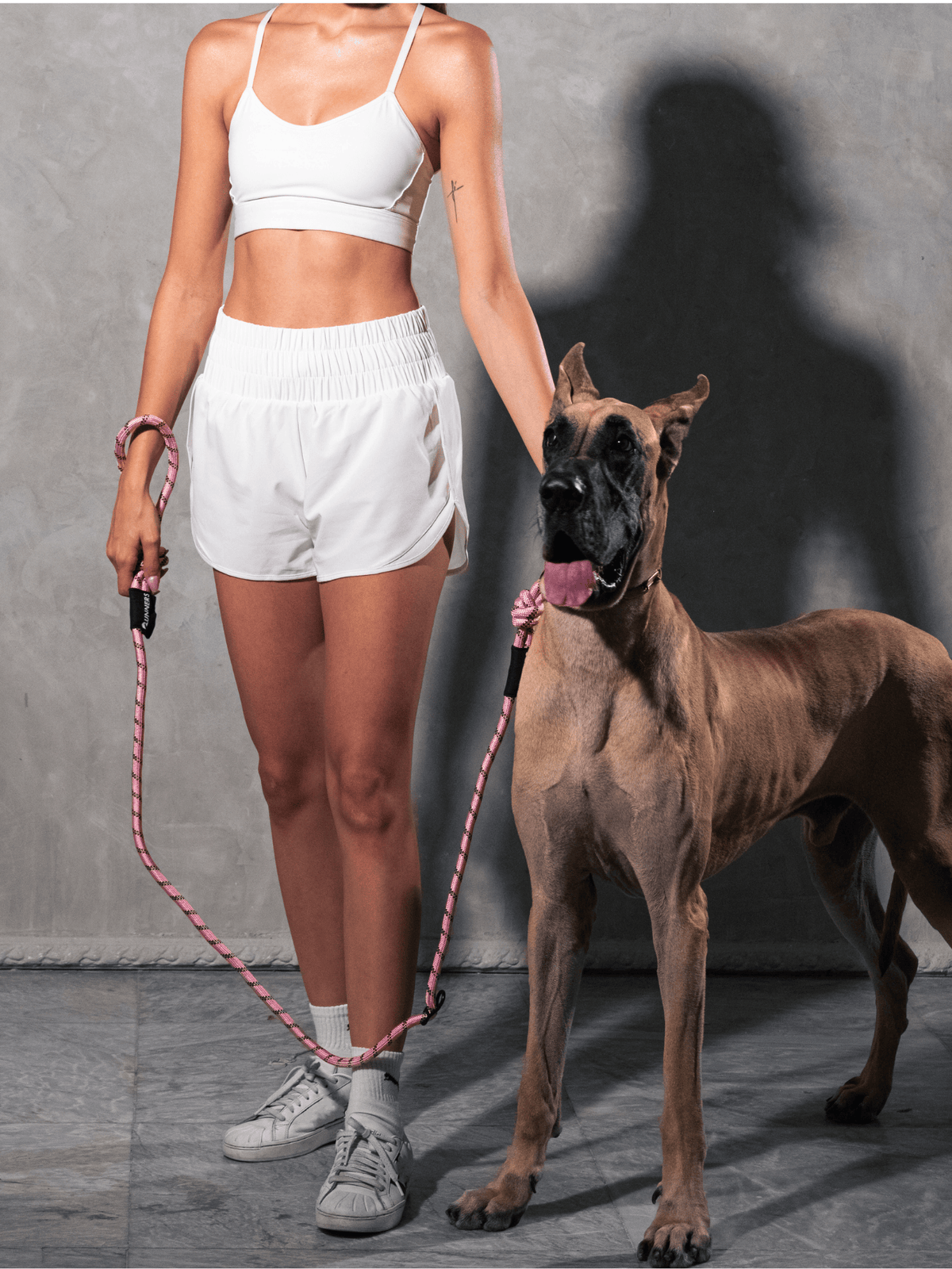 Woman in white workout attire holding pastel pink hands-free dog leash connected to Great Dane - Runner's Athletics