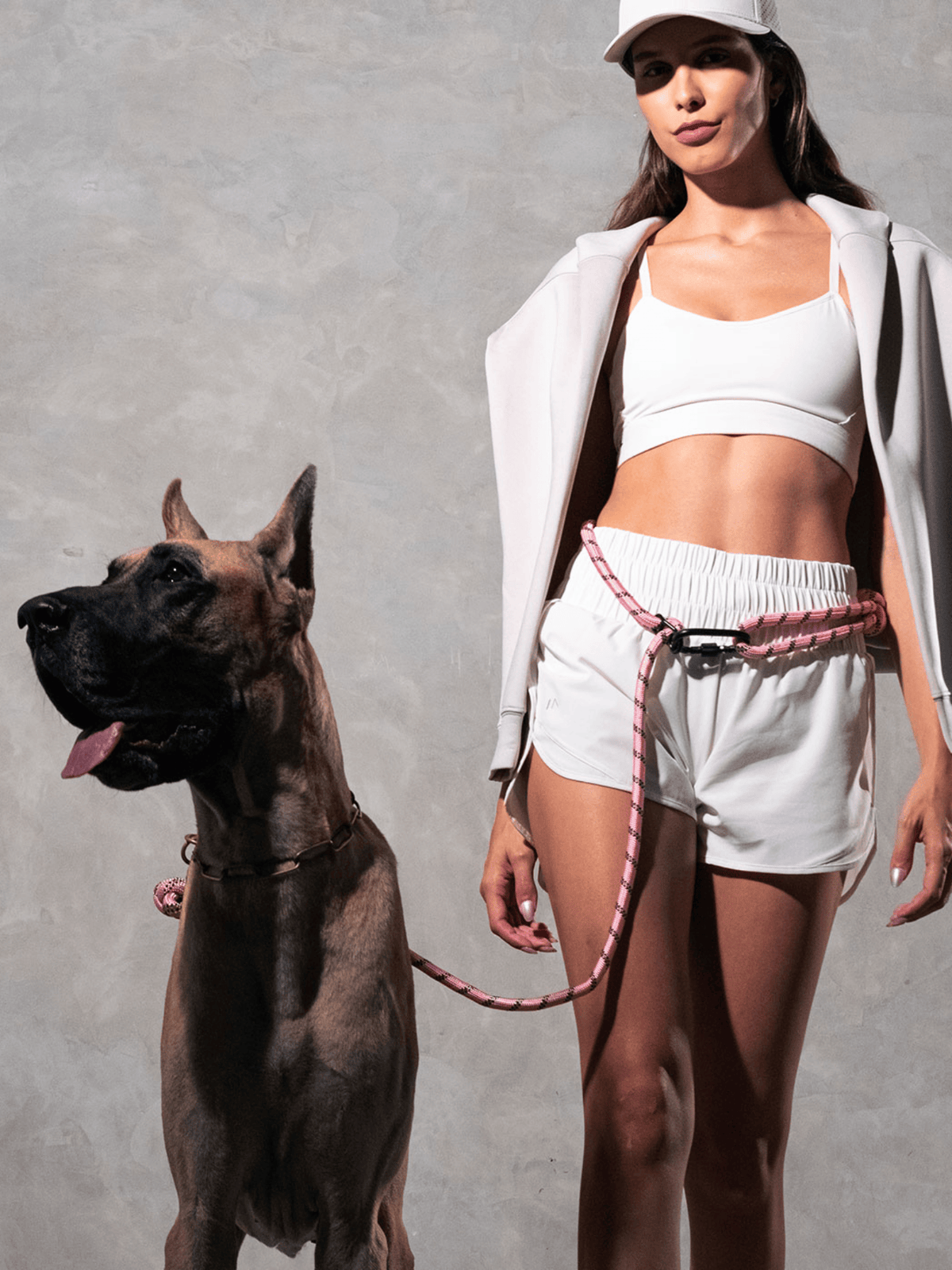 Woman in white athletic wear with pastel pink hands-free dog leash attached to waist belt, standing beside Great Dane - Runner's Athletics