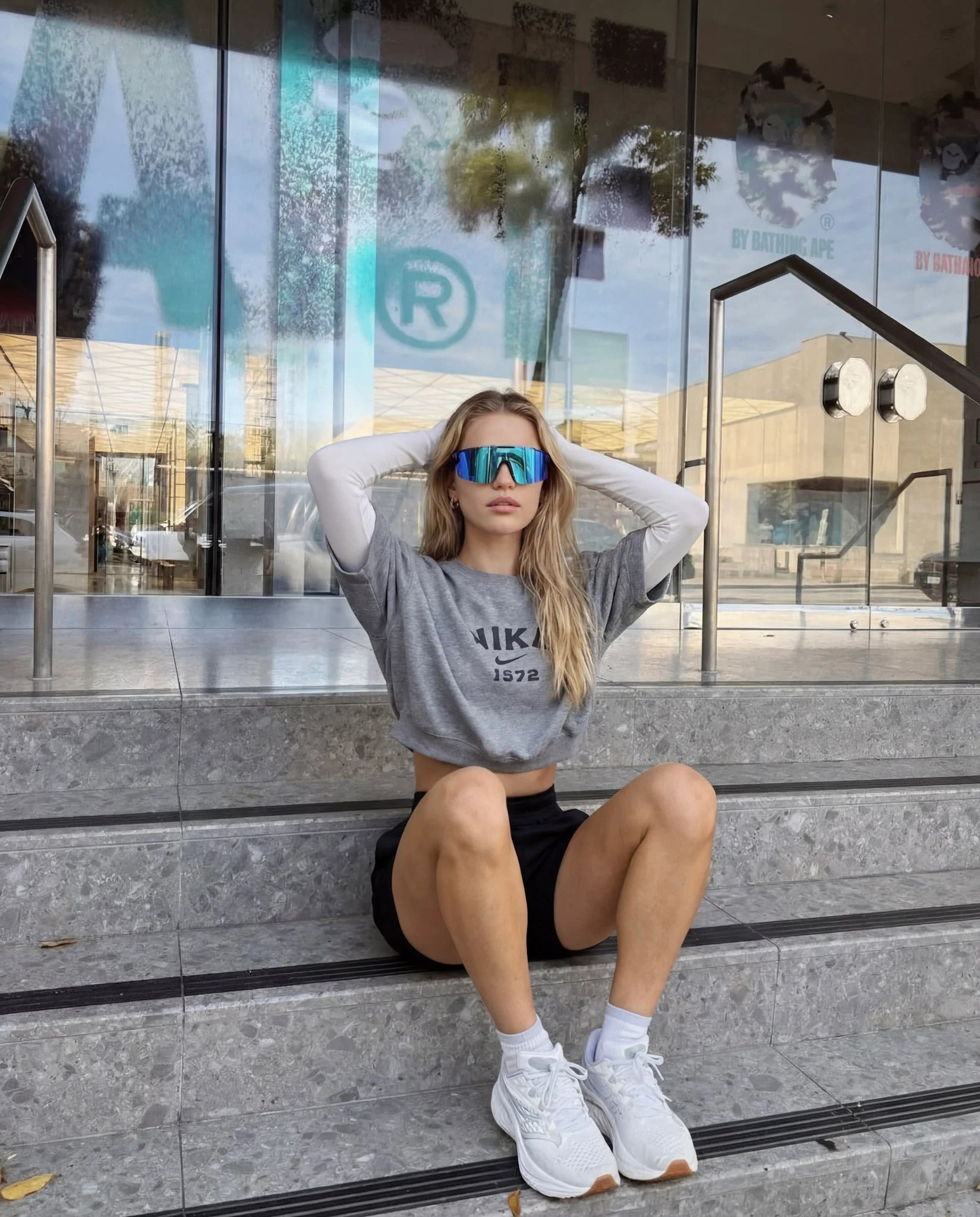 Woman wearing ice blue polarized running sunglasses seated outdoors in street style look