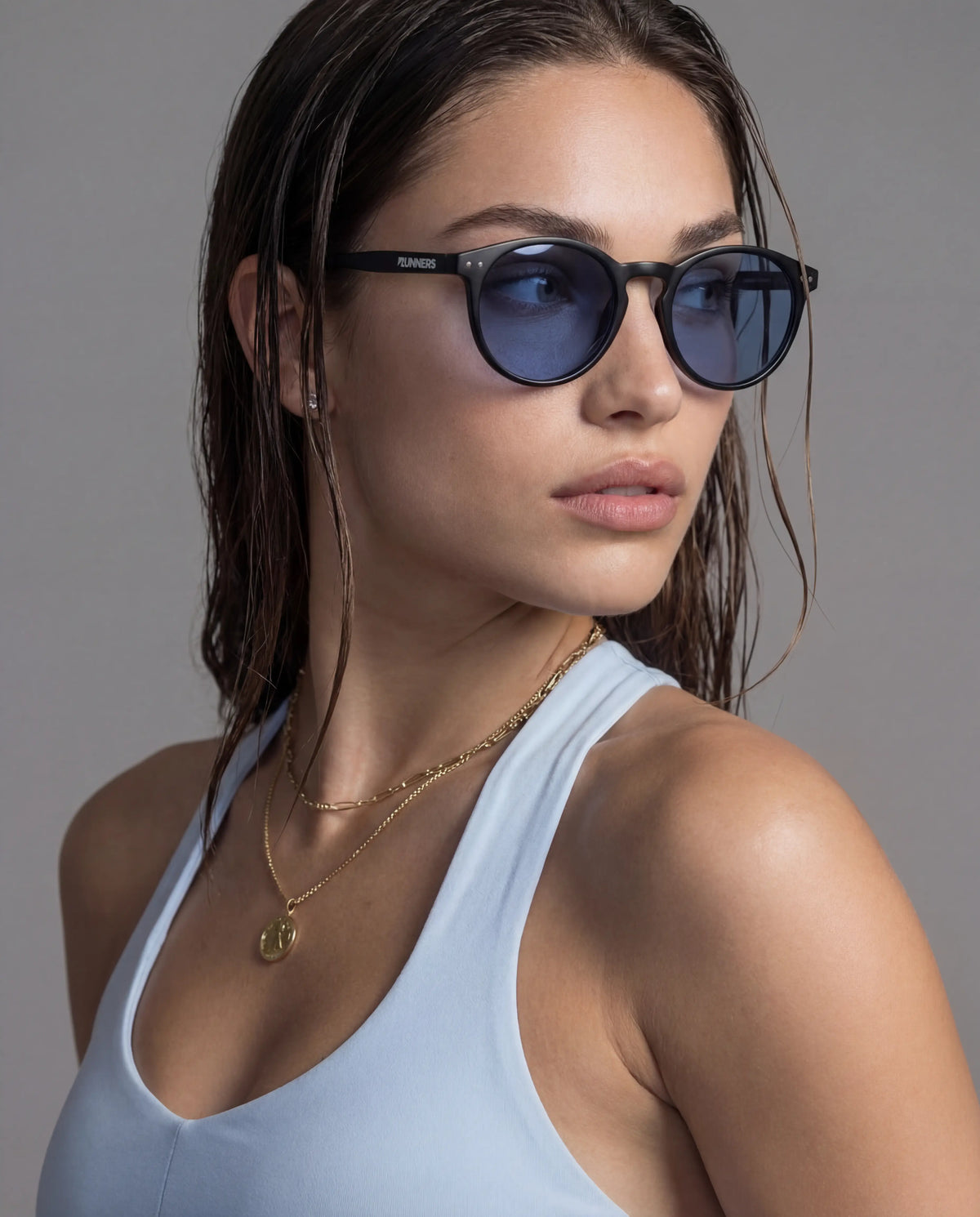 Black round running sunglasses with blue lenses on woman in light blue sports bra