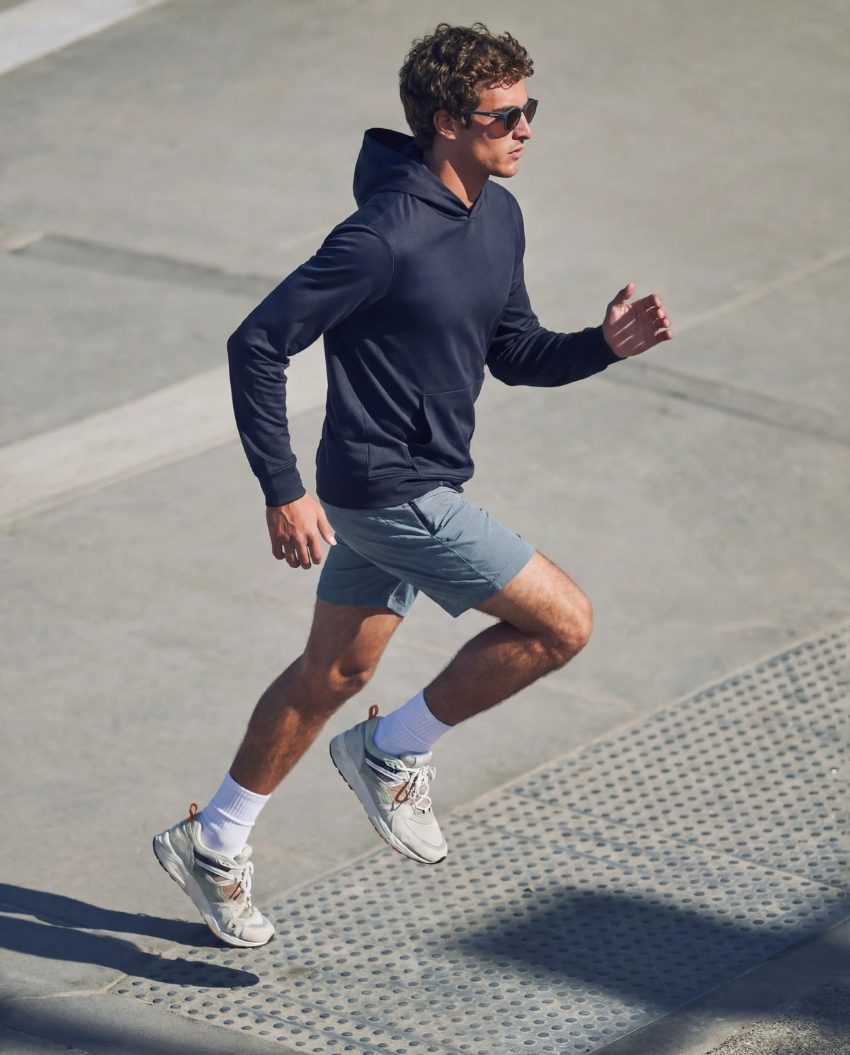 Black round running sunglasses on man from Runners Athletics running on outdoor steps in navy hoodie