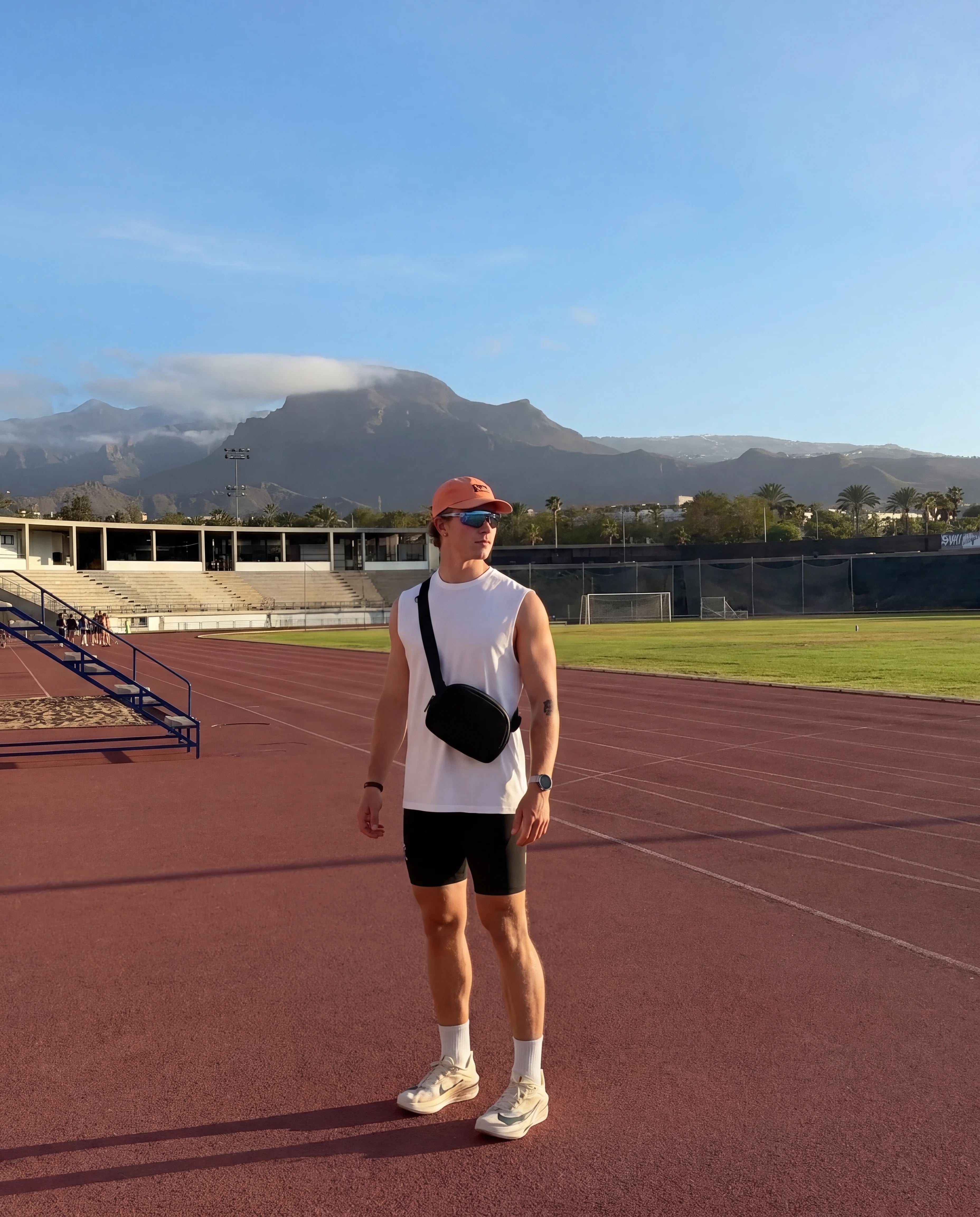 Black sling bag crossbody worn on athletics track with mountain backdrop