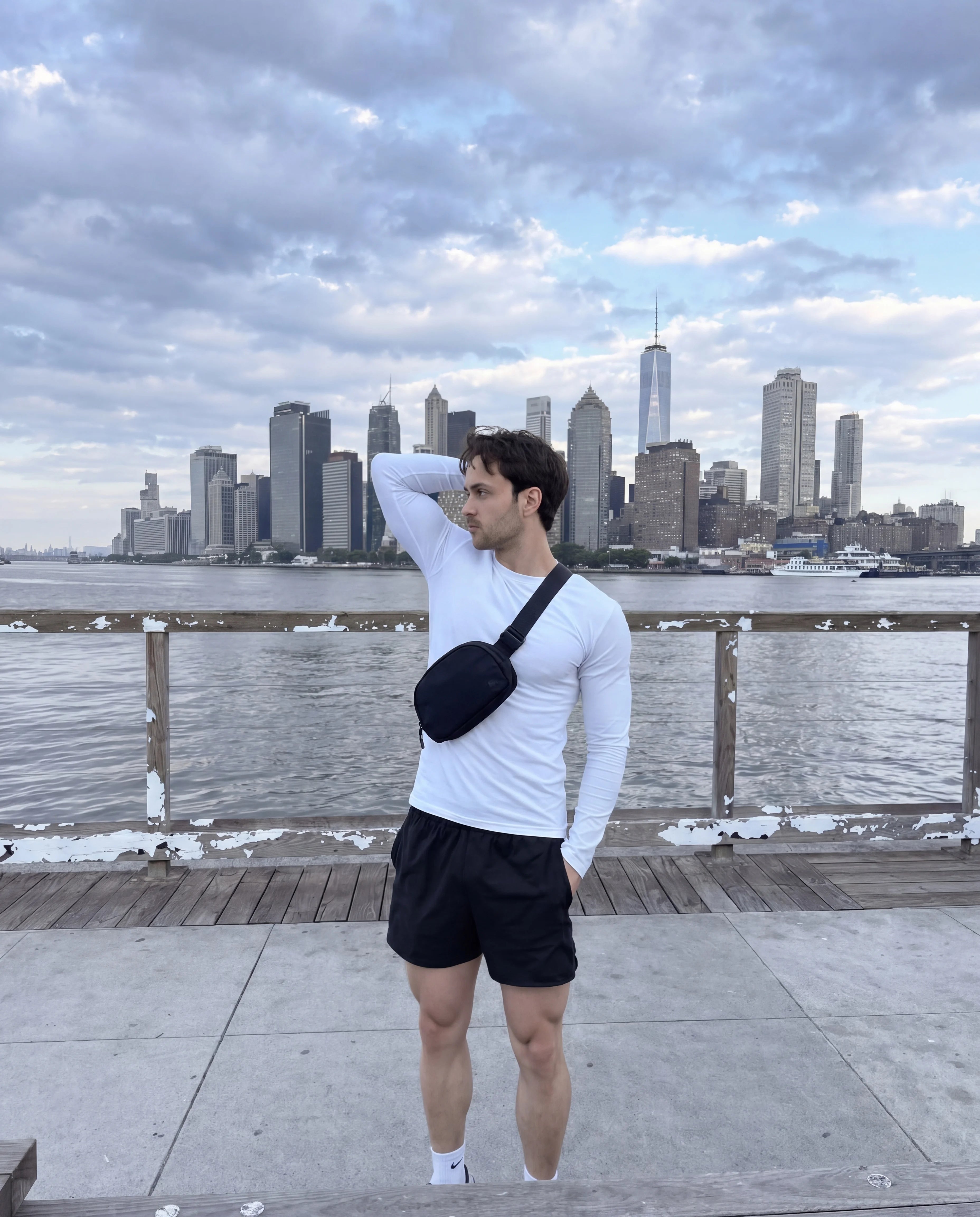 Black crossbody sling bag worn by man at NYC waterfront skyline view