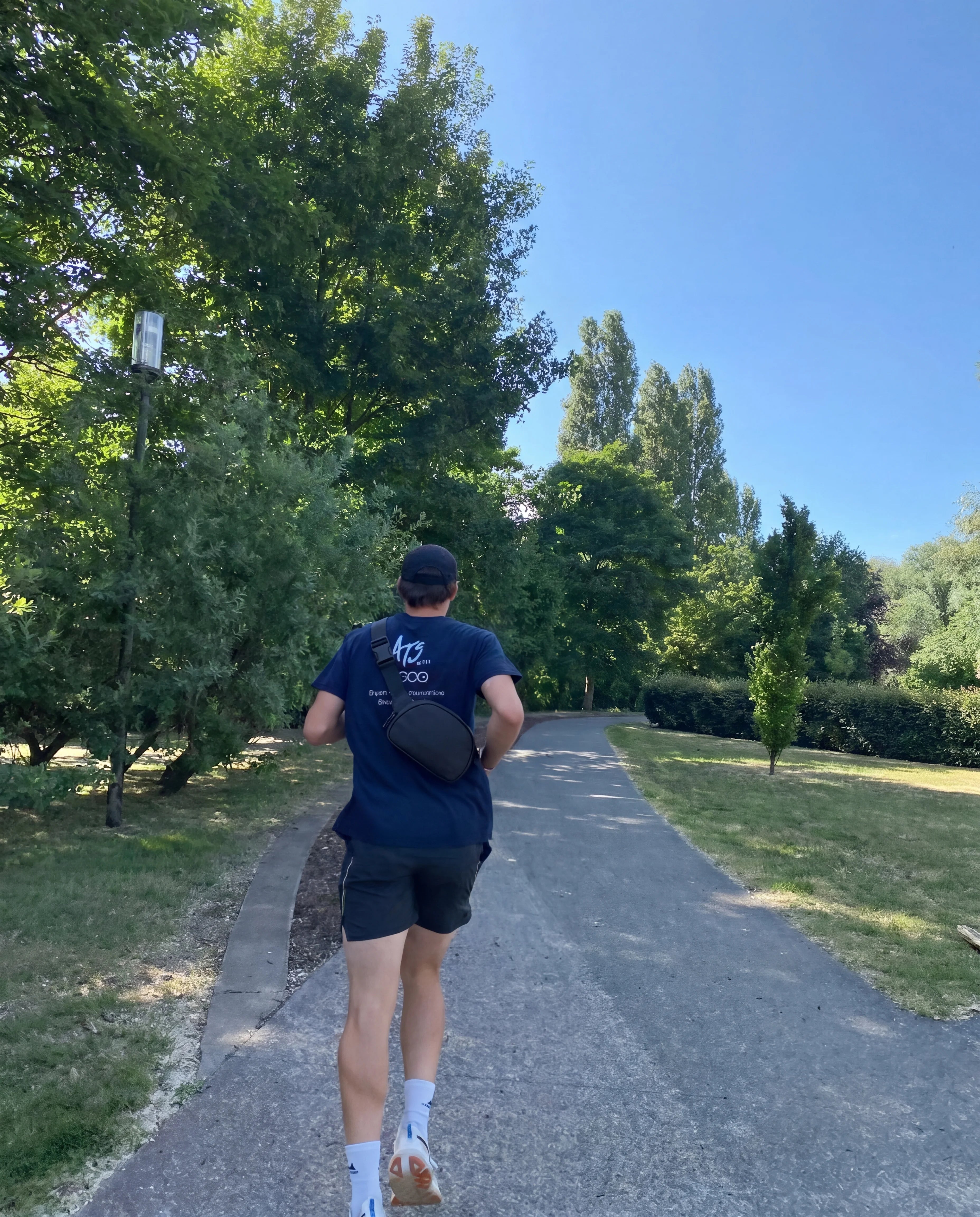 Black crossbody sling bag worn by man running on park path back view