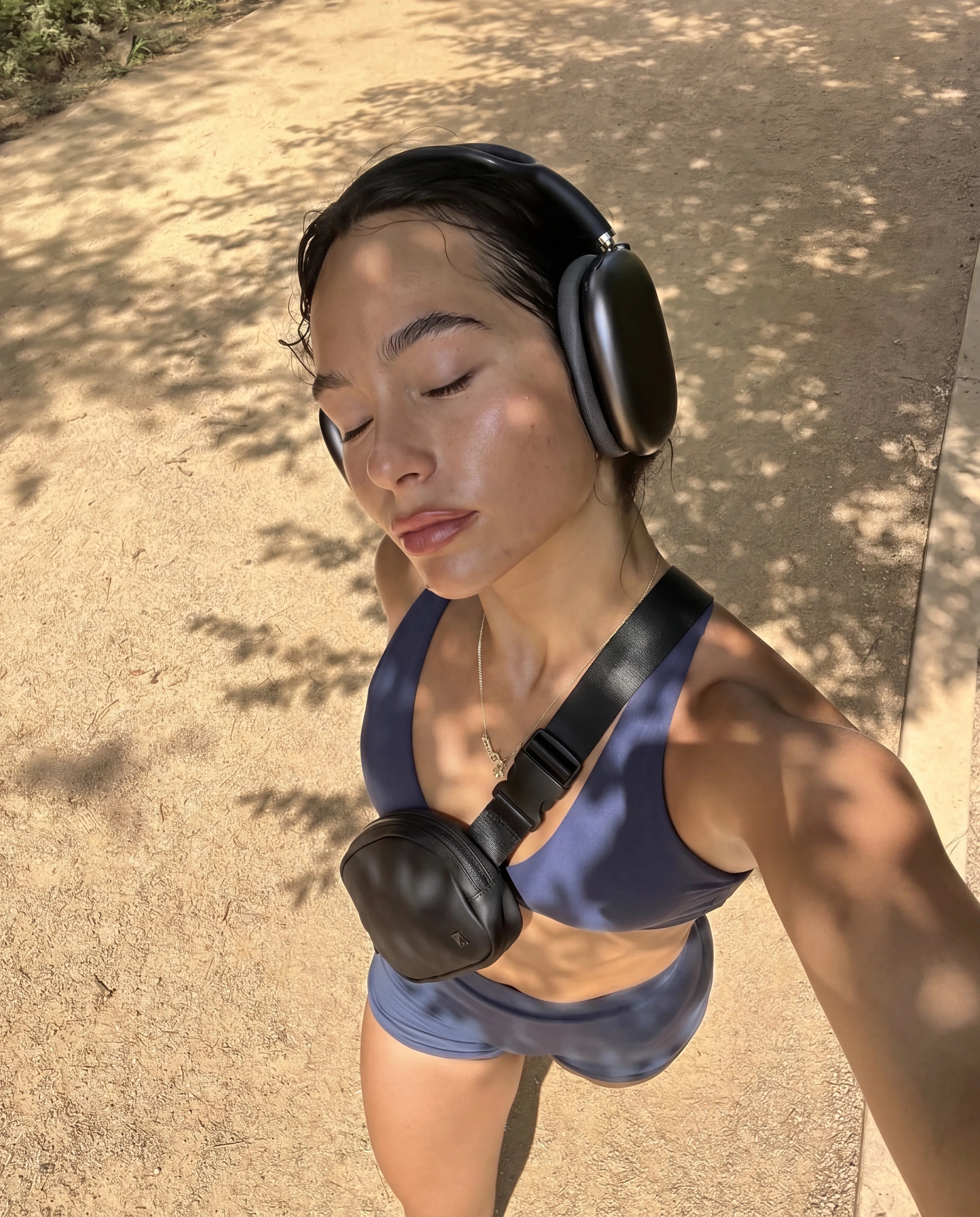 Black sling bag worn crossbody with blue sports bra on sunny outdoor path