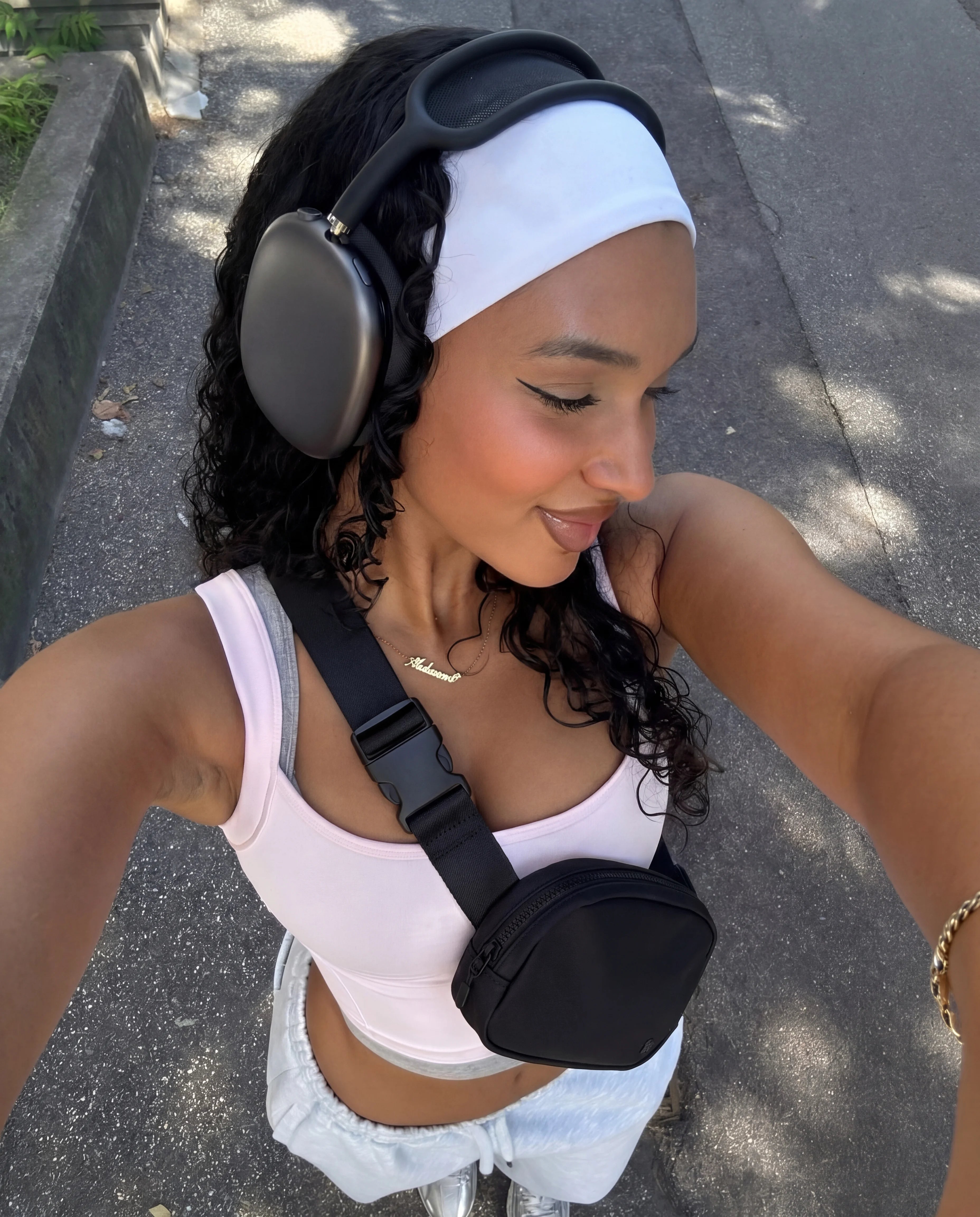 Black sling bag crossbody worn with pink sports bra on park path walk