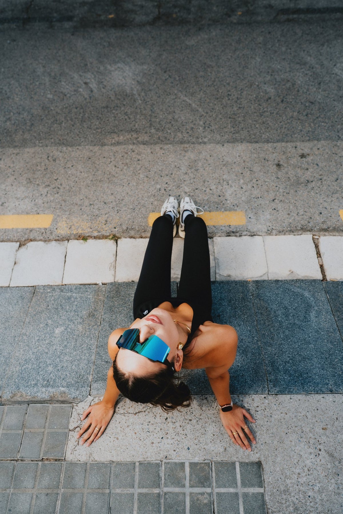Woman in black Runner's Athletics tank, leggings and X365 sunglasses sitting on a city street
