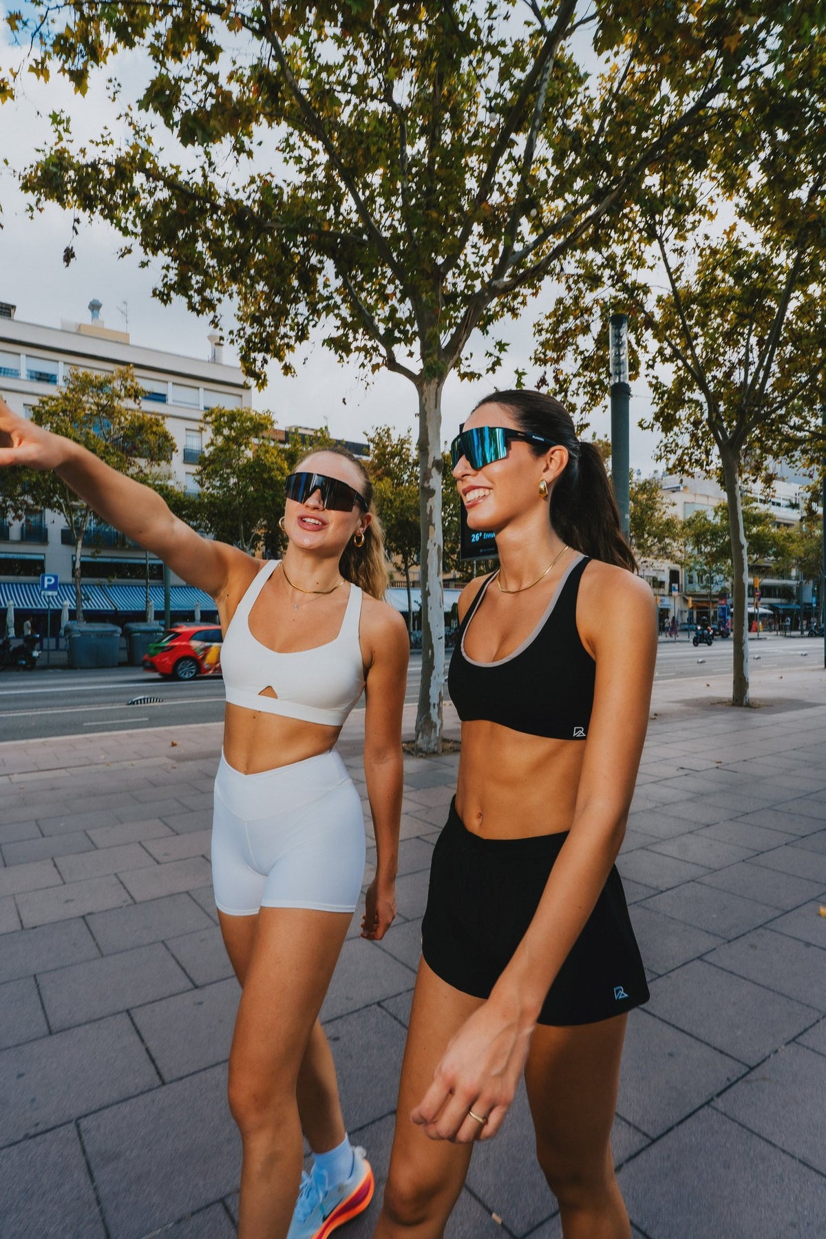 Two women in white and black Runner's Athletics sports bras and shorts walking in the city