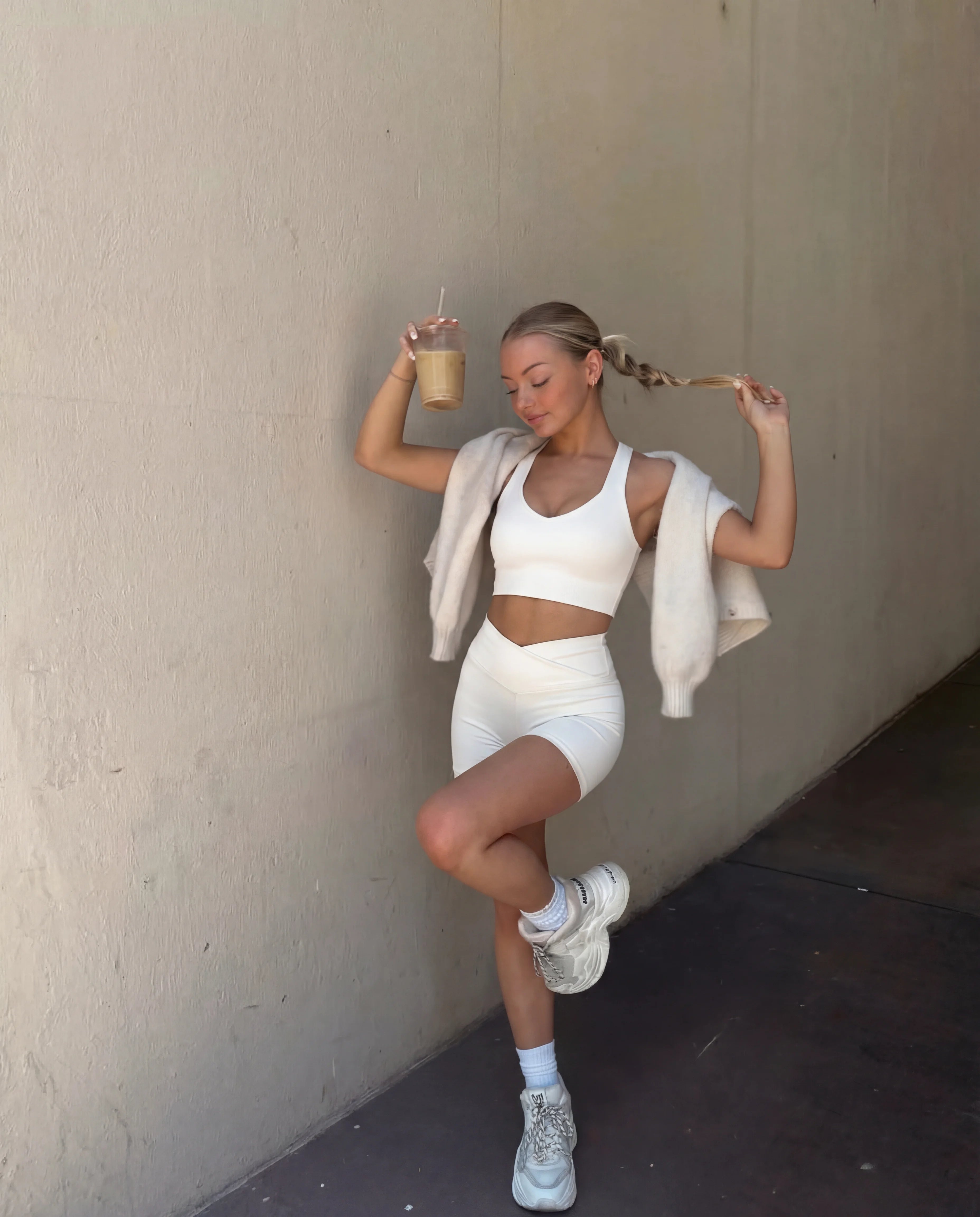 Beige workout set functional tank and sculpting shorts worn outdoors holding iced coffee