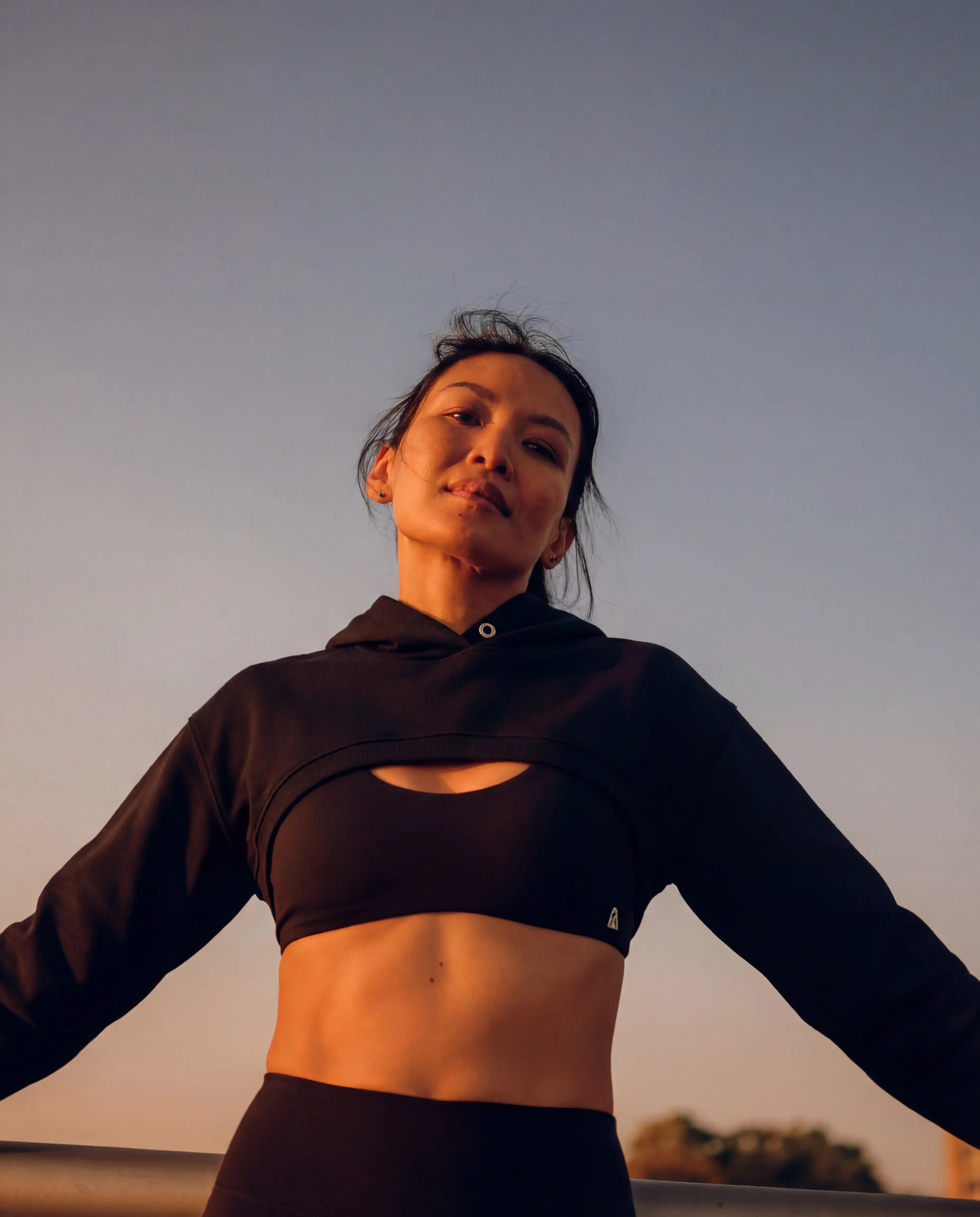 Black workout set strappy sports bra and cropped hoodie worn outdoors at sunset