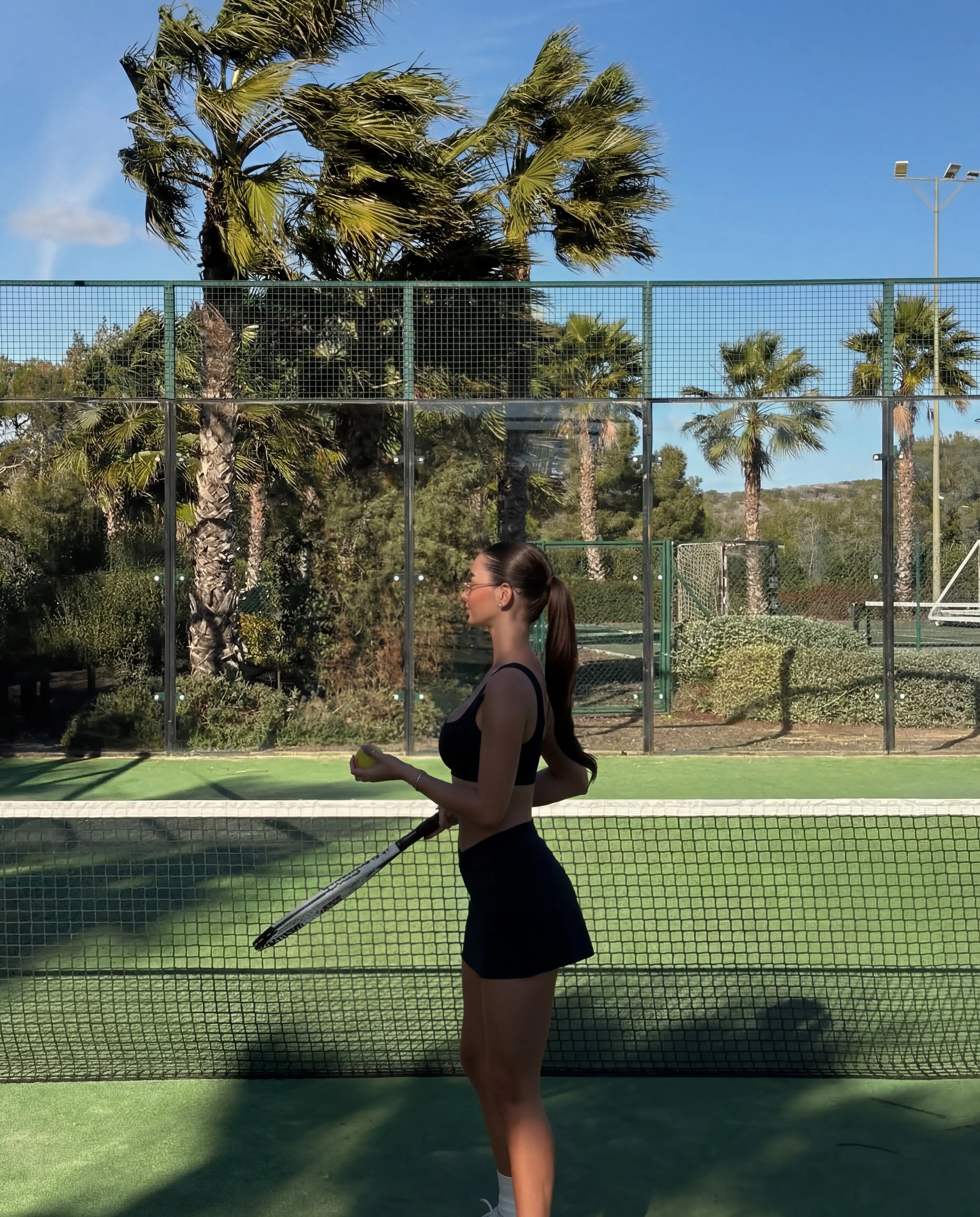 Black workout set sports bra and tennis skort worn on outdoor tennis court